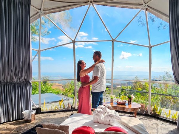 Pareja abrazada dentro del domo panoramico con globos de corazon, cama y vista amplia al valle