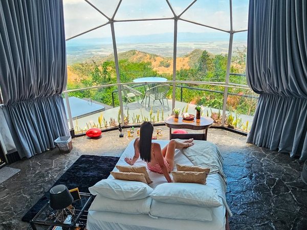 Mujer recostada en la cama del domo panoramico contemplando el valle por el ventanal.