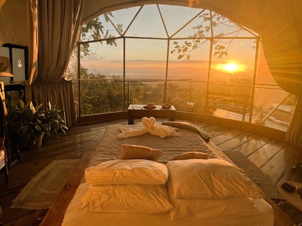 Cama con cisnes de toalla frente al frente de ventanas geodesicas del domo panoramico al amanecer.