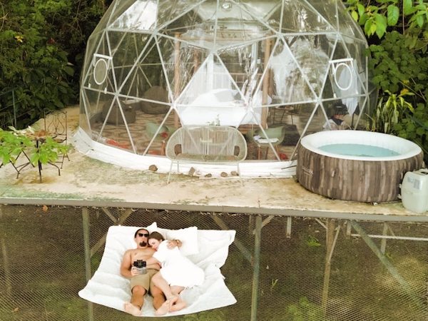 Vista elevada del domo transparente con jacuzzi inflable y pareja recostada en la red catamaran