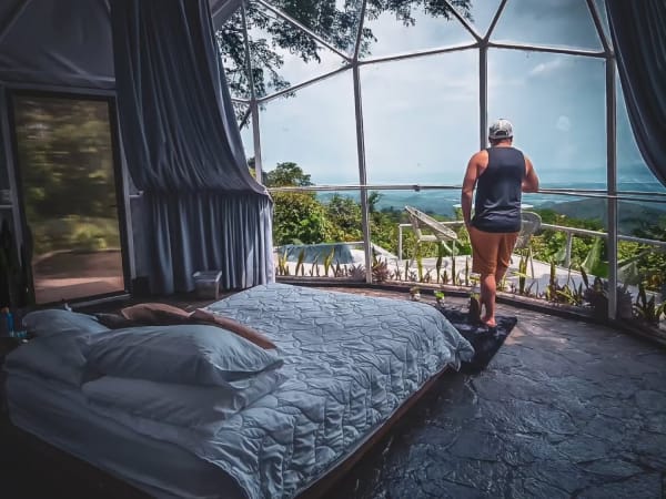 Hombre contemplando la vista al valle desde el interior del domo panoramico junto a la cama