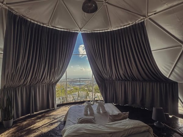 Cama con toallas en forma de cisne dentro del domo panoramico con cortinas y ventanal con vista.
